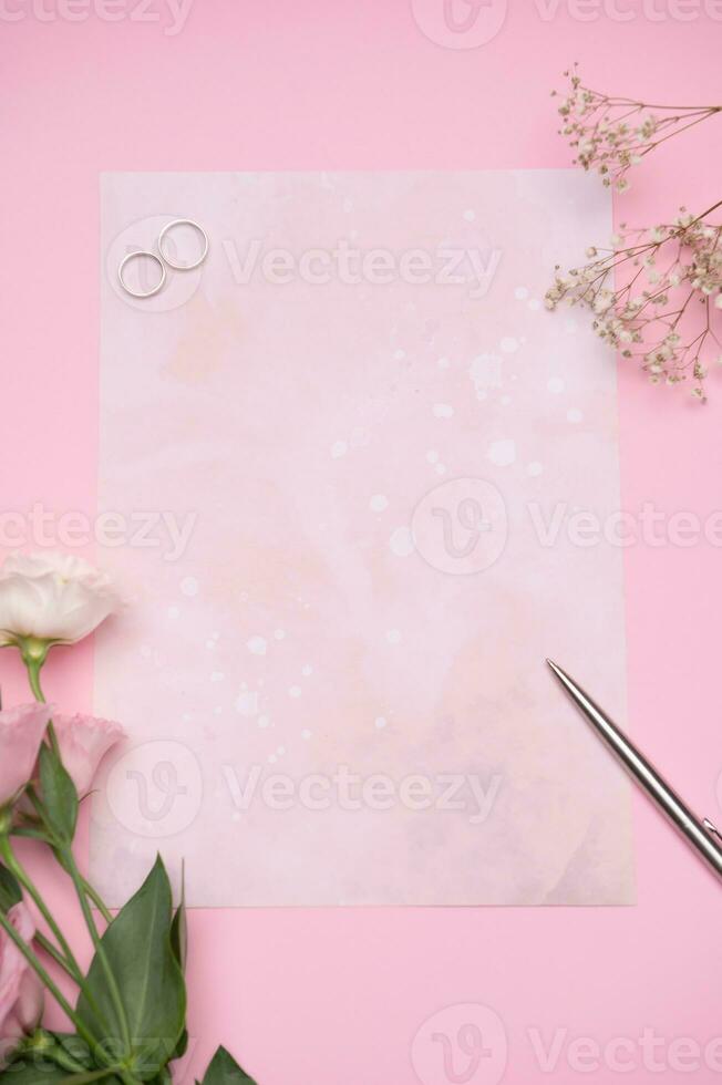 de concept van uitnodiging voor feestelijk evenement. bruiloft ringen Aan roze brief papier met kopiëren ruimte en bloemen arrangement foto