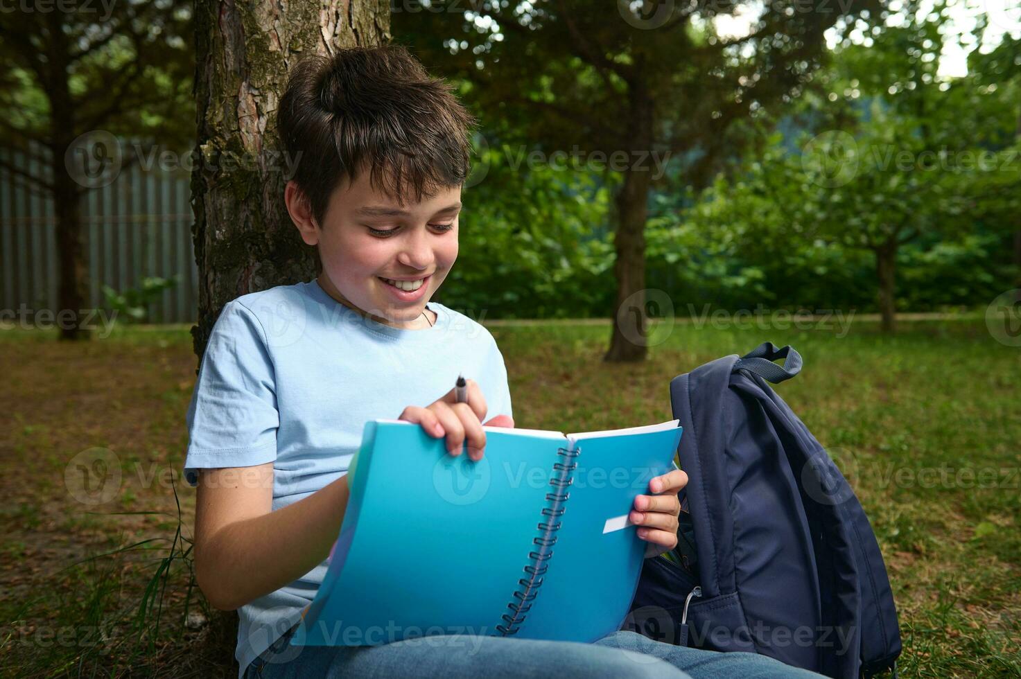 detailopname portret van een gelukkig glimlachen spaans tiener- schooljongen aan het doen huiswerk buitenshuis, Holding een potlood en schrijfboek. foto