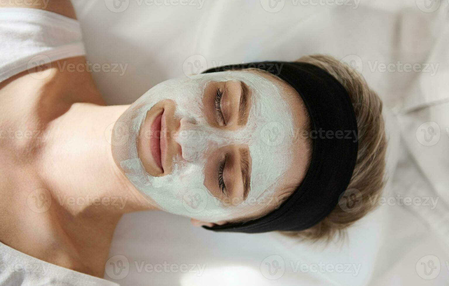 top visie van een gelukkig jong vrouw met een schoonheid masker Aan haar gezicht ontspannende en genieten van schoonheid procedure in spa salon foto