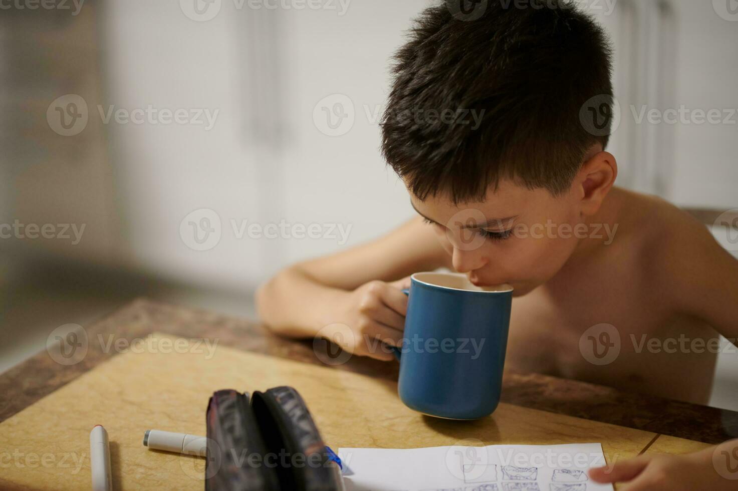 schattig jongen zittend Bij tafel en drinken thee foto