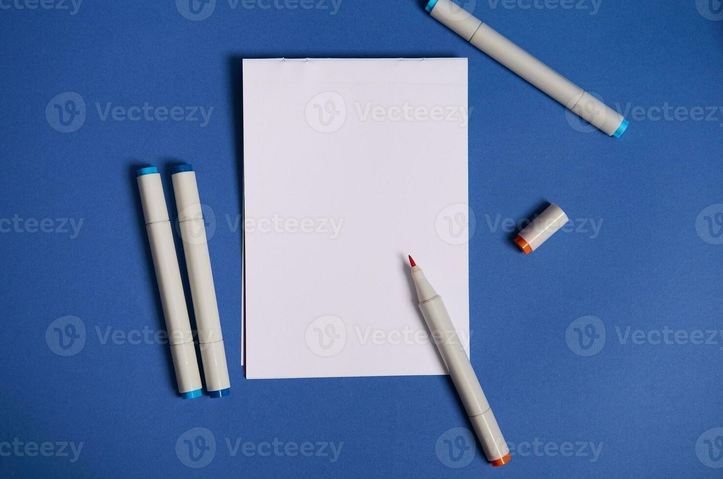 tweekleurig vlak leggen samenstelling met waterverf markeringen of viltstift pennen met wit blanco vel van papier met kopiëren ruimte geïsoleerd Aan blauw achtergrond. foto
