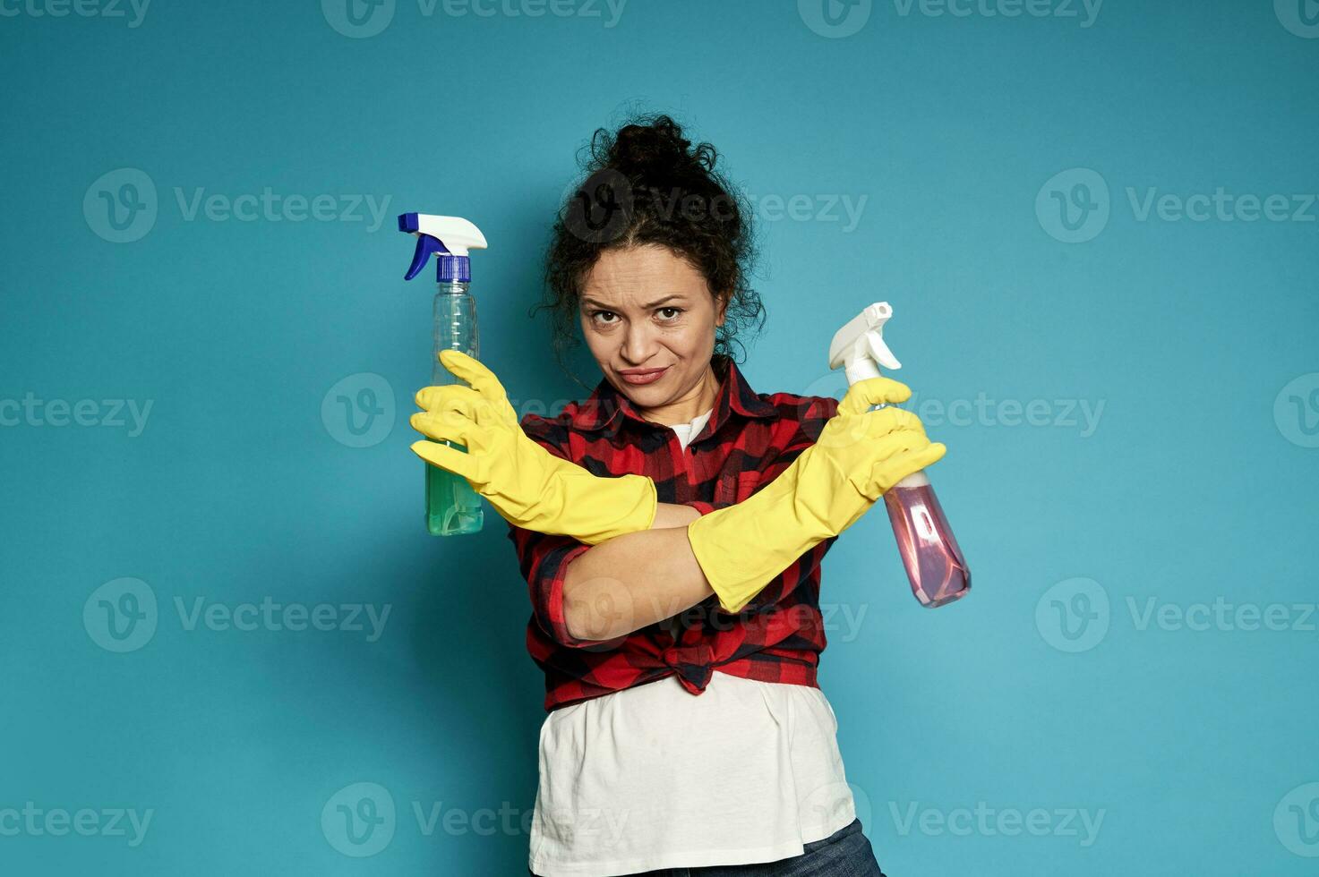 jong moe uitgeput ontevreden huisvrouw gekruiste haar armen in ontkenning, met schoonmaak sprays in handen foto