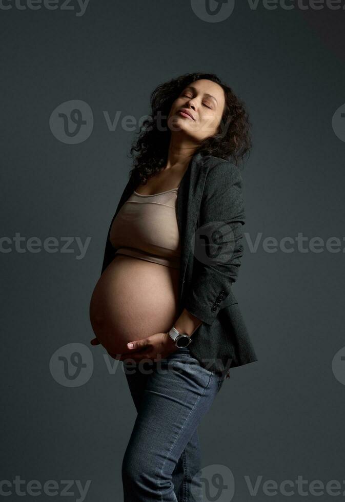 studio portret van een verrukkelijk prachtig zwanger vrouw Holding haar buik, geïsoleerd grijs achtergrond. mooi zwangerschap foto