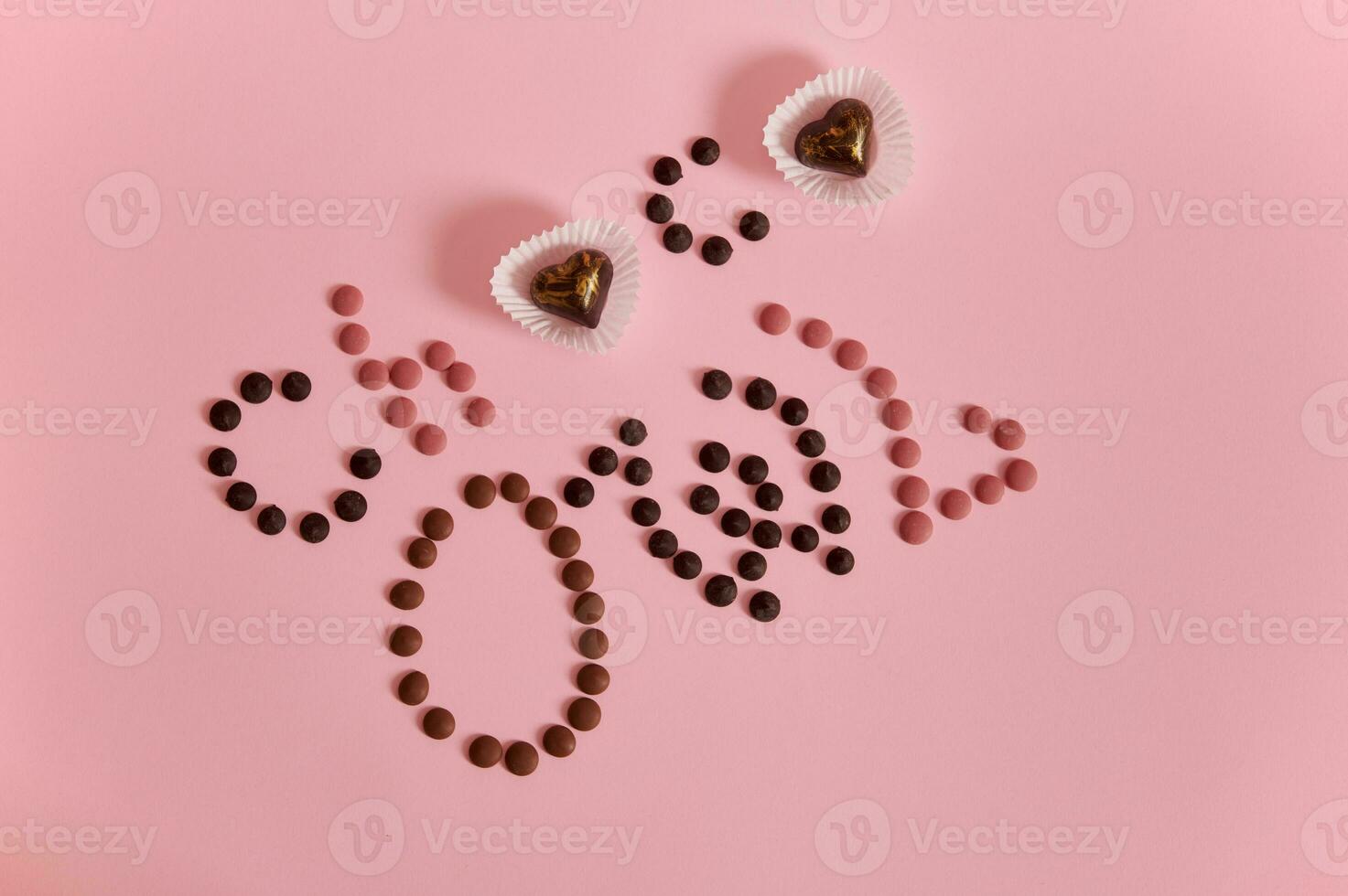 vlak leggen van opschrift belettering gelegd uit van multi gekleurde chocola pillen en pralines Aan roze achtergrond met kopiëren ruimte foto