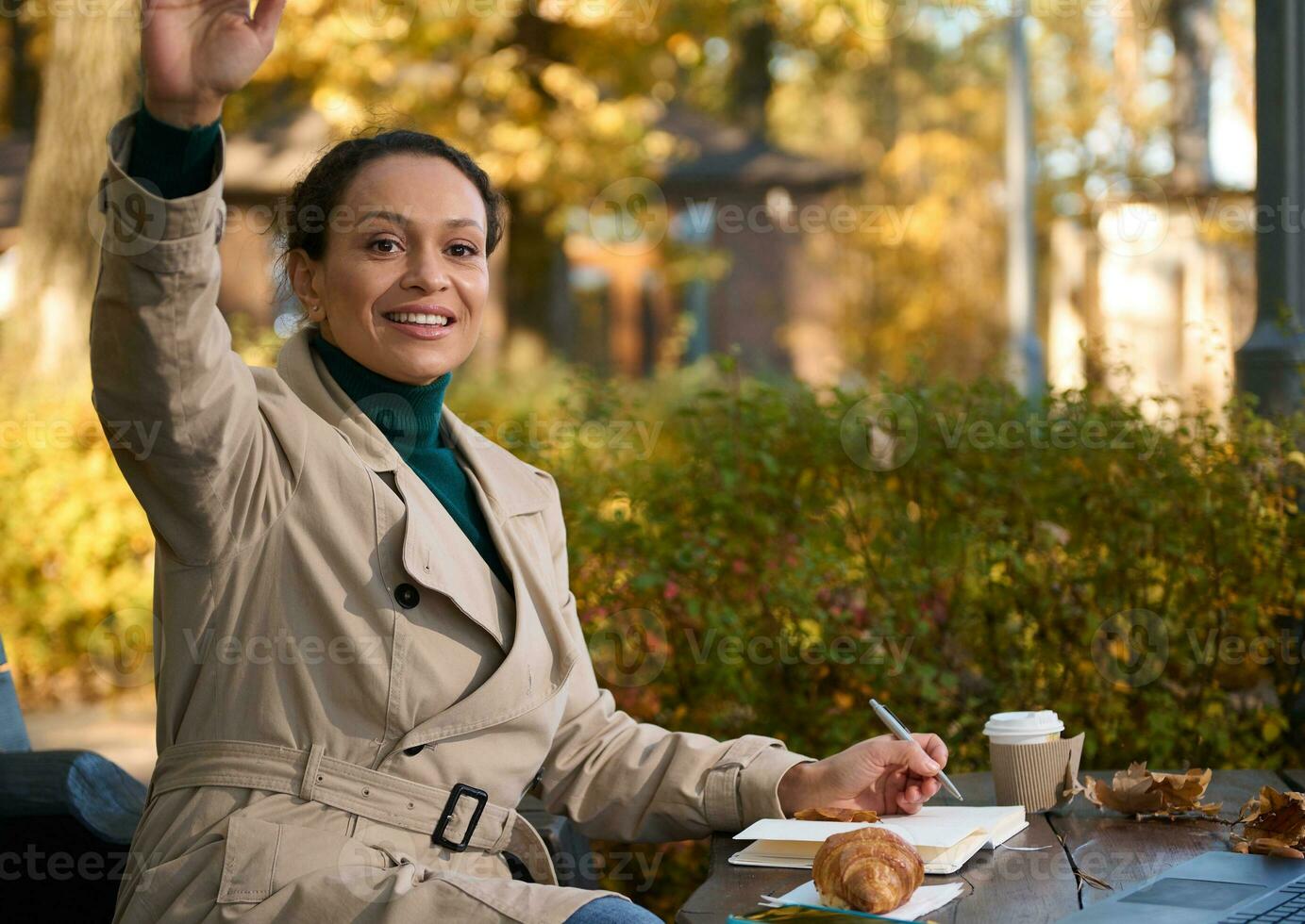 detailopname portret van een charmant bedrijf vrouw, jong freelancer zittend in een cafe en maken een Mark in een wekelijks, beven haar hand- in de richting van de gesprekspartner en glimlachen Bij hem foto