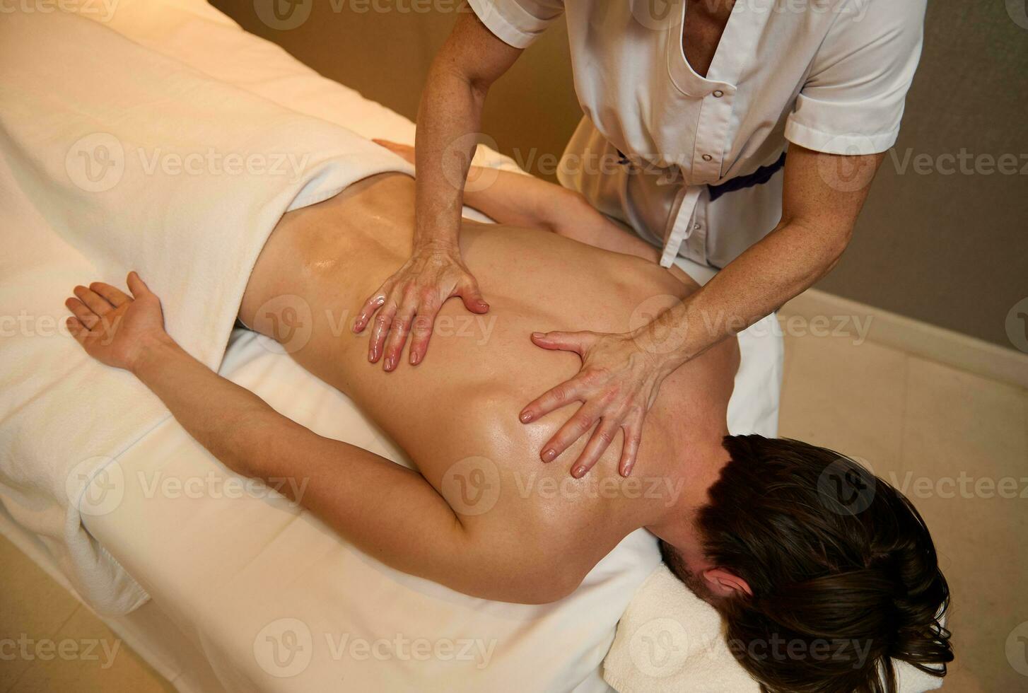 top visie van onherkenbaar professioneel masseuse geven medisch behandeling massage naar jong man's terug spieren ontspannende Aan massage tafel Bij Gezondheid spa centrum. ayurvedisch en alternatief behandeling concept foto