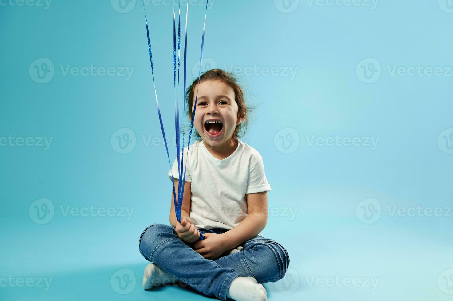 voorkant visie van een schattig meisje lachend en Holding touw van ballonnen zittend Aan blauw achtergrond foto