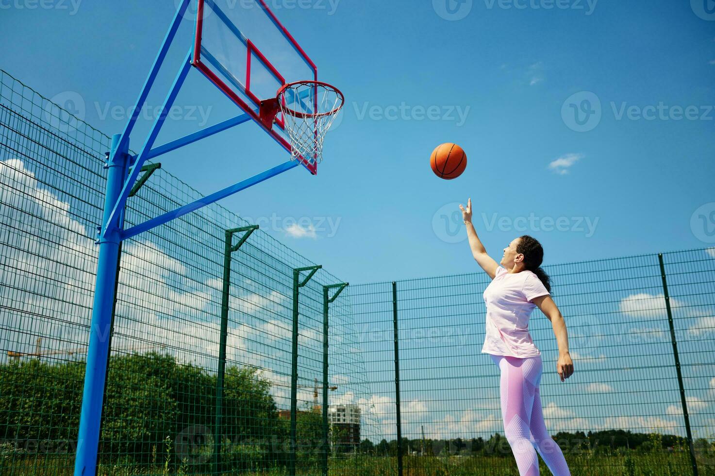 jong vrouw spelen basketbal Aan de rechtbank buitenshuis en het werpen de bal in de hoepel foto