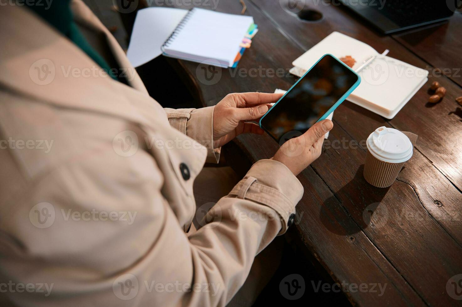 onherkenbaar persoon handen gebruik makend van een slim telefoon met blanco zwart scherm voor kopiëren ruimte Aan de achtergrond van een houten tafel met Open kladblok en schrijfboek en heerlijk ontbijt foto