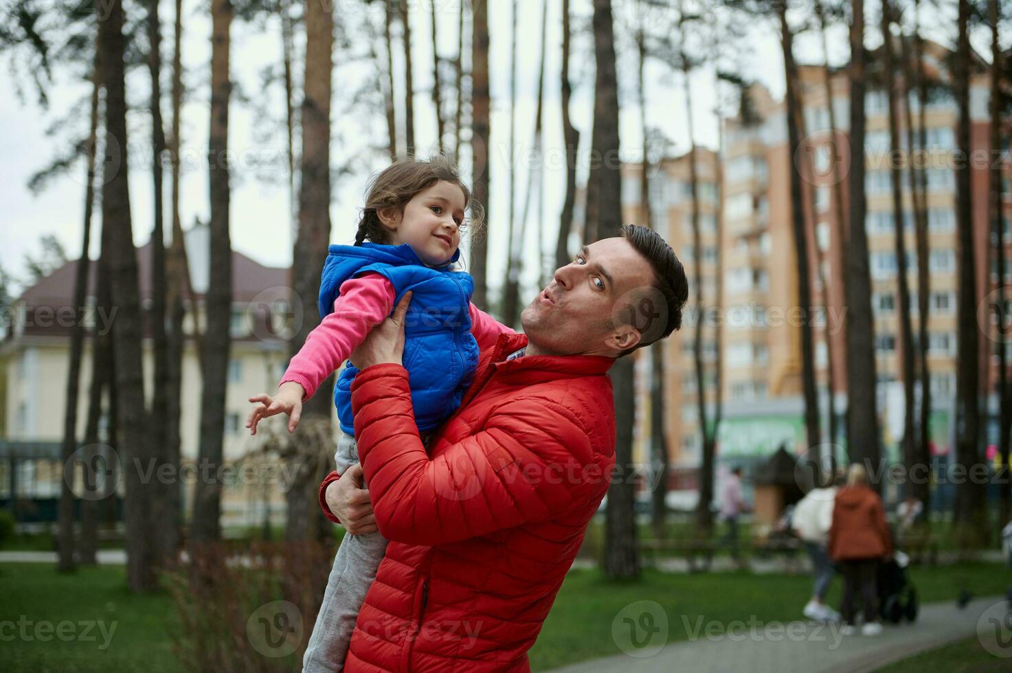 knap Kaukasisch Mens - liefhebbend vader gooit zijn dochter - een weinig schattig meisje hoog omhoog in een stad park. familie en vader dag, liefde, ouders, kinderen foto