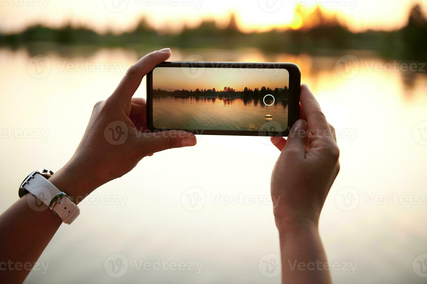 detailopname van handen nemen een fotografie van een mooi zonsondergang Aan de oever van het meer achtergrond. zomer thema's. mobiel telefoon in leven visie foto