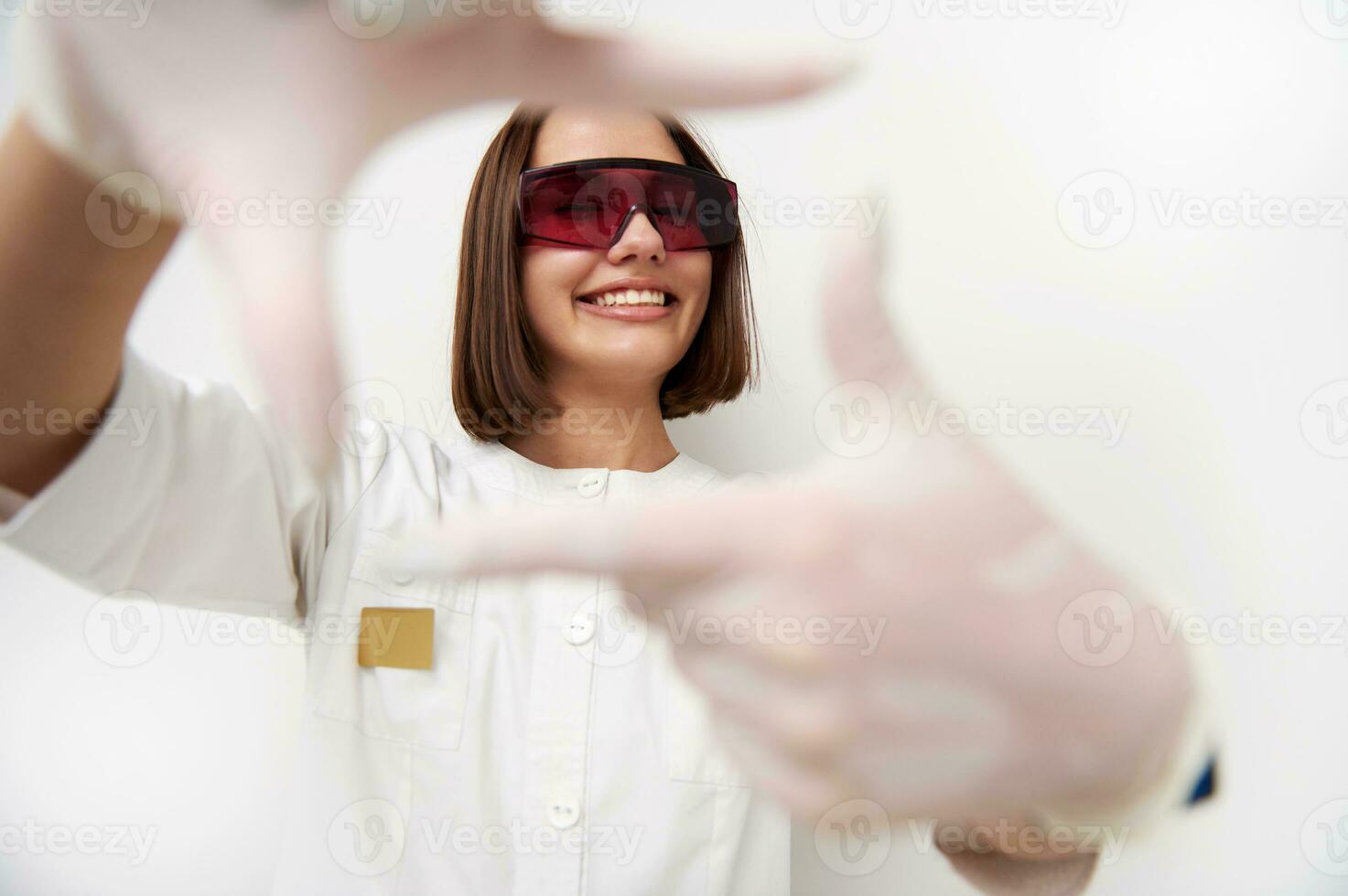 gelukkig vrouw dokter glimlachen met toothy glimlach terwijl op zoek door haar vingers kader foto