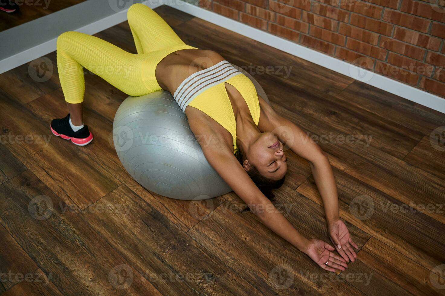 hoog hoek visie van een jong vrouw uitrekken haar lichaam aan het liegen Aan een geschiktheid bal gedurende kruis training. pilates, fitheid, uitrekken en actief levensstijl concept foto