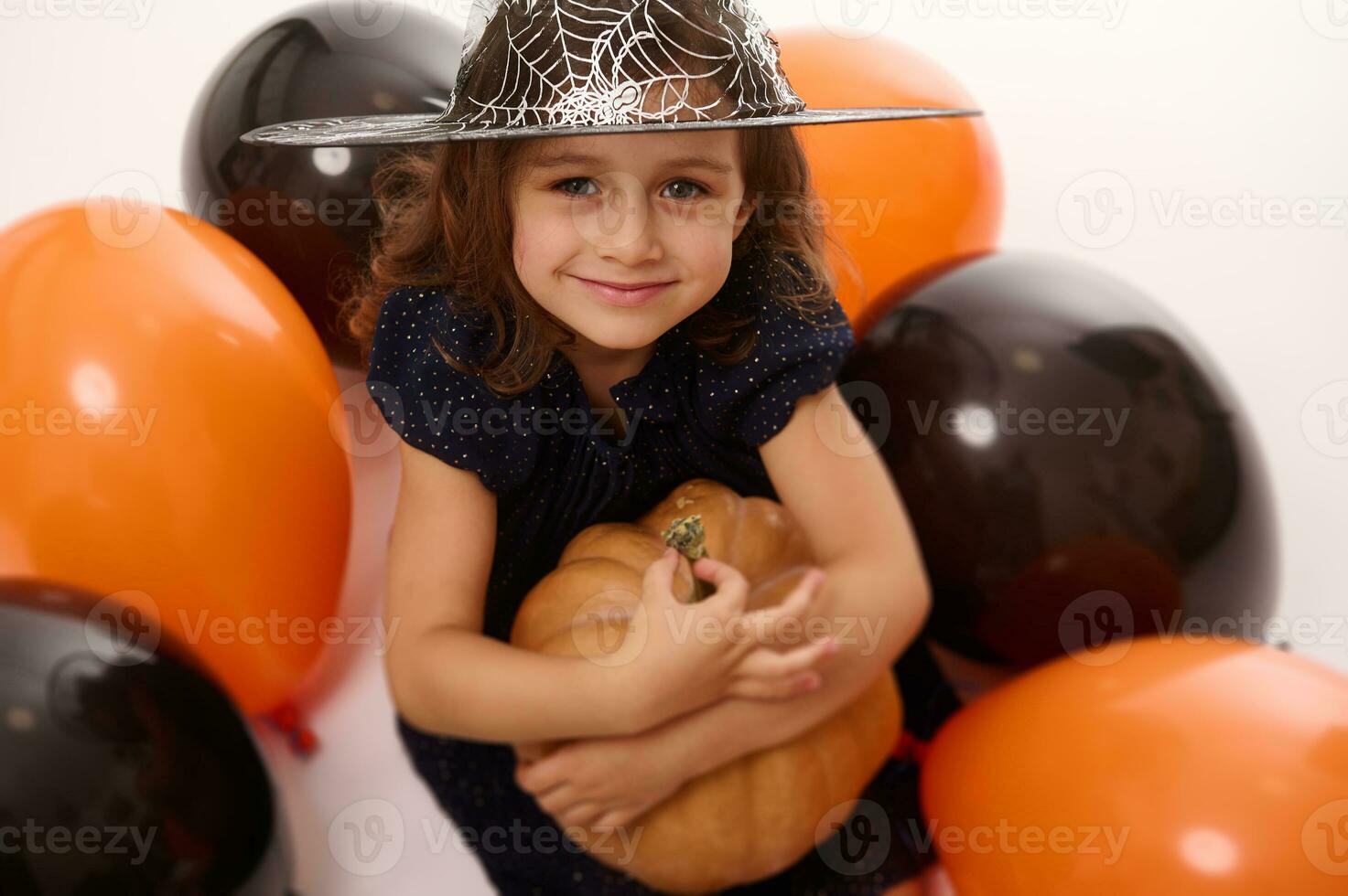 4 jaren oud weinig meisje in heks kostuum en tovenaar hoed Toneelstukken met ballonnen en een pompoen geïsoleerd Aan wit achtergrond. concept van een kind hebben pret Bij halloween partij foto