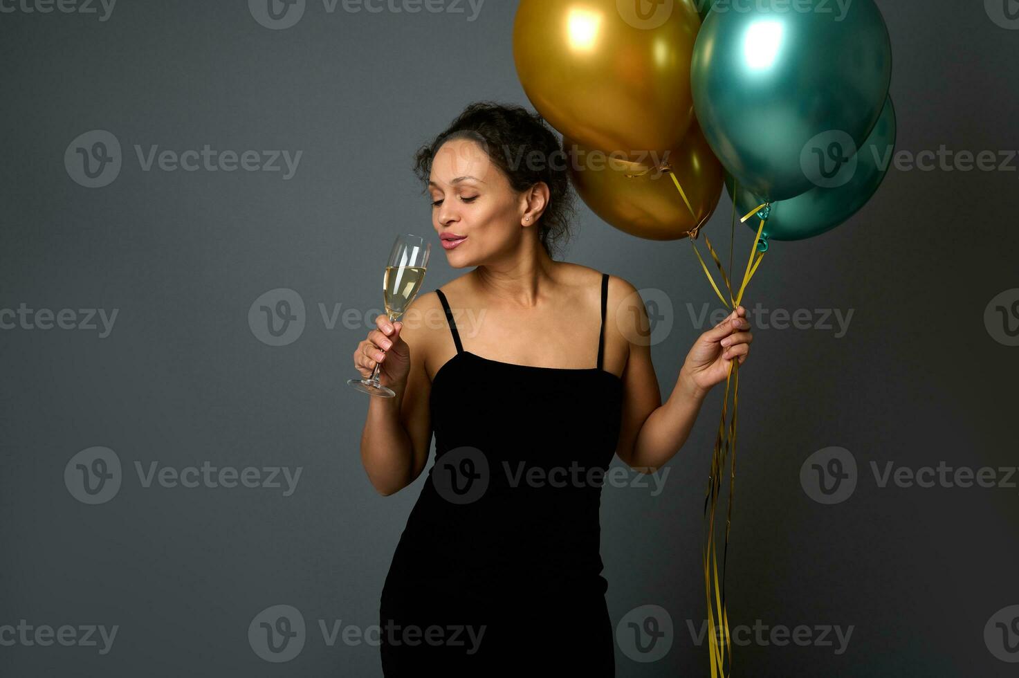 aantrekkelijk sexy vrouw in avond jurk houdt feestelijk glimmend lucht ballonnen en drankjes sprankelend wijn van glas geïsoleerd over- grijs achtergrond met kopiëren ruimte voor kerstmis, nieuw jaar of verjaardag advertentie foto