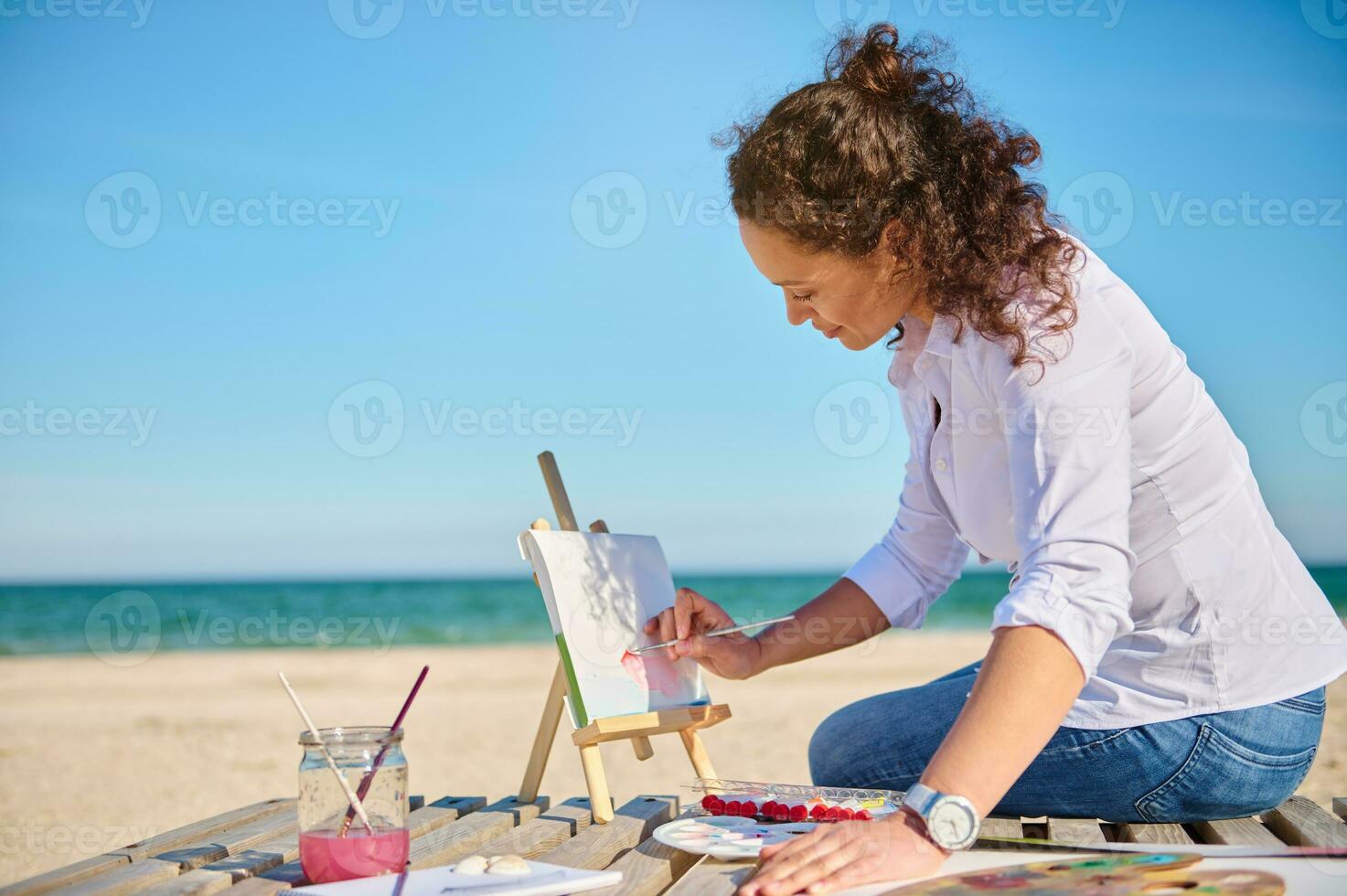 volwassen vrouw schilder genieten van schilderij Aan canvas buitenshuis Aan de zee achtergrond. foto