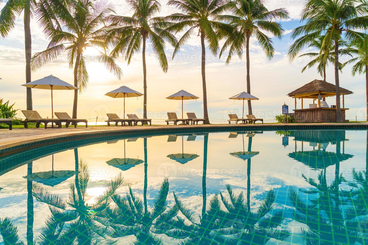 mooie luxe parasol en stoel rond buitenzwembad in hotel en resort met kokospalm op zonsondergang of zonsopgang foto