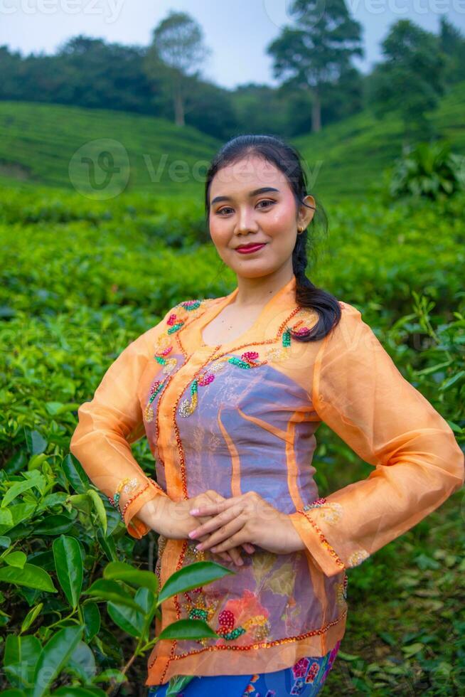 een thee blad boer in een oranje jurk poseren in voorkant van een heel mooi thee tuin foto