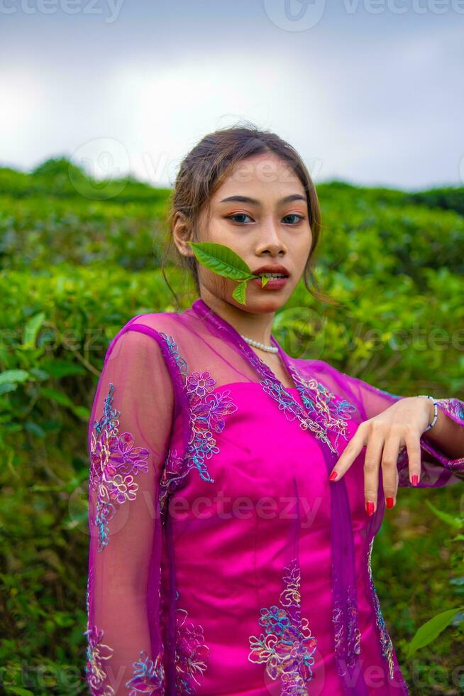 een Aziatisch vrouw in een roze jurk is staand in voorkant van een thee tuin foto