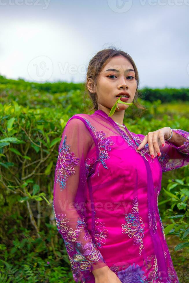 een Aziatisch vrouw in een roze jurk is staand in voorkant van een thee tuin foto