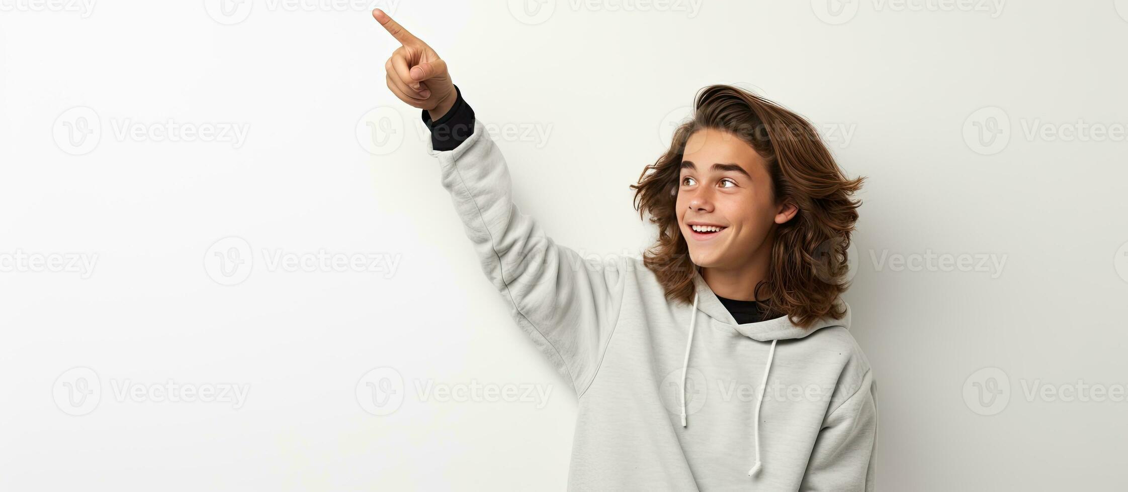 gelukkig tiener jongen met lang haar- poseren Bij een studio gebaren een nieuw idee terwijl een vent points omhoog Bij leeg ruimte foto