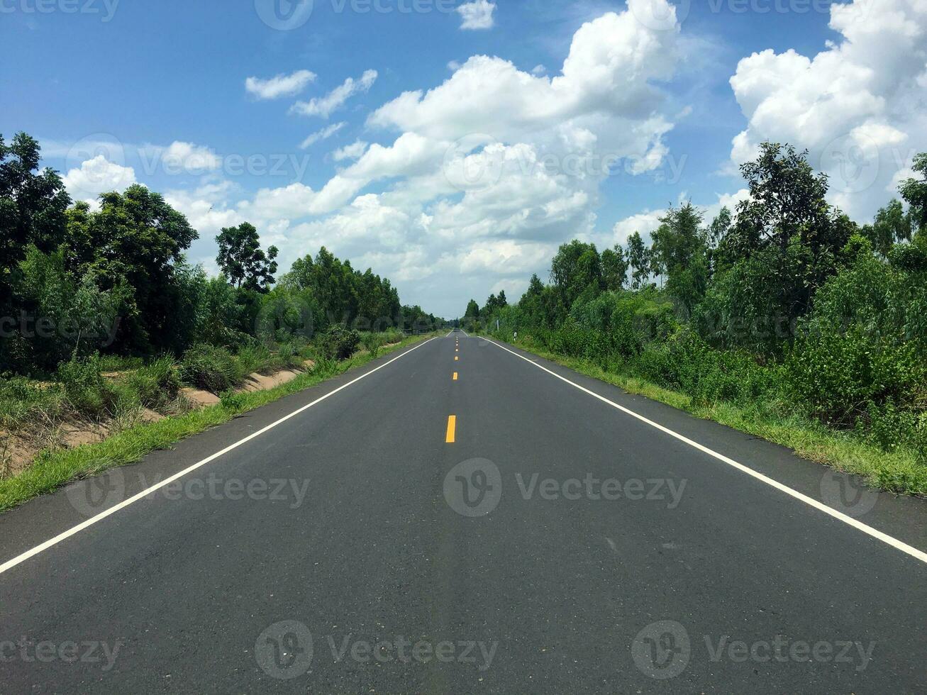 beeld van nieuw geplaveid weg in de dag in de platteland geschilderd geel verdelen lijn met bomen, gras langs de weg, lucht met wit wolken foto