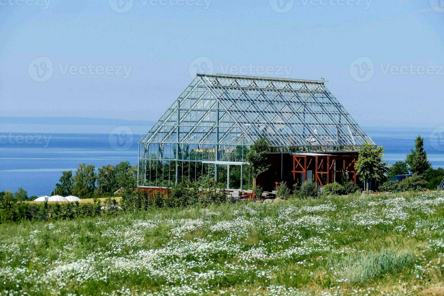 een glas huis in de midden- van een veld- met de zee in de achtergrond foto
