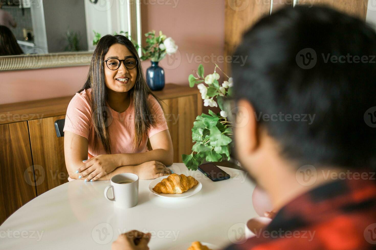 jong verschillend liefhebbend paar aan het eten croissant en praat samen Bij huis in ontbijt tijd. communicatie en verhouding concept foto