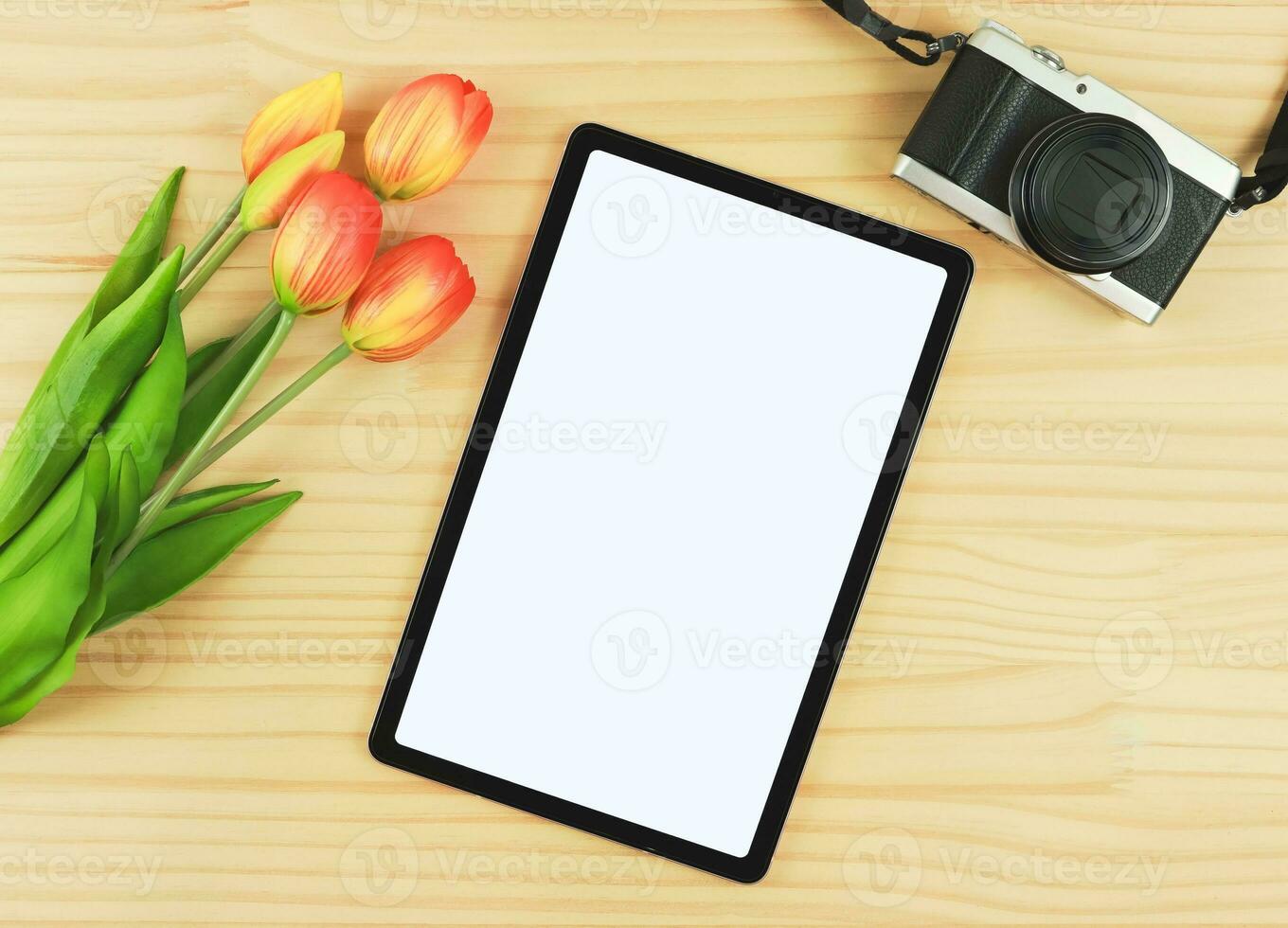 vlak leggen van digitaal tablet met blanco wit scherm, tulp bloemen en digitaal camera geïsoleerd Aan houten tafel achtergrond. foto