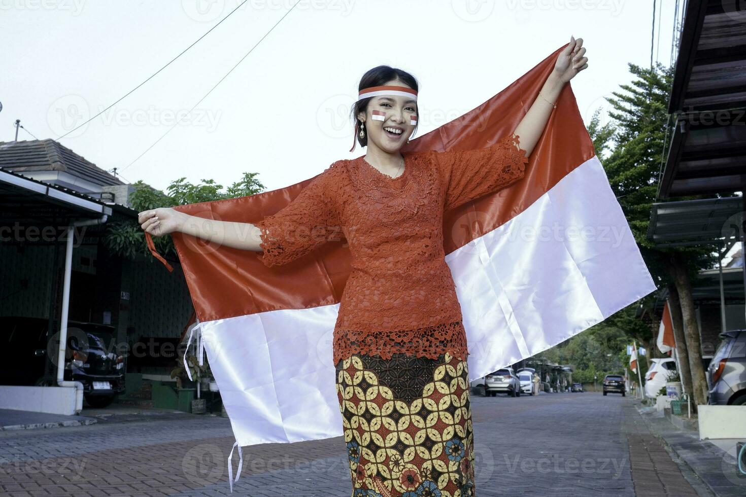 gelukkig glimlachen Indonesisch vrouw vervelend rood kebaya Holding Indonesië's vlag naar vieren Indonesië onafhankelijkheid dag. buitenshuis fotoshoot concept foto