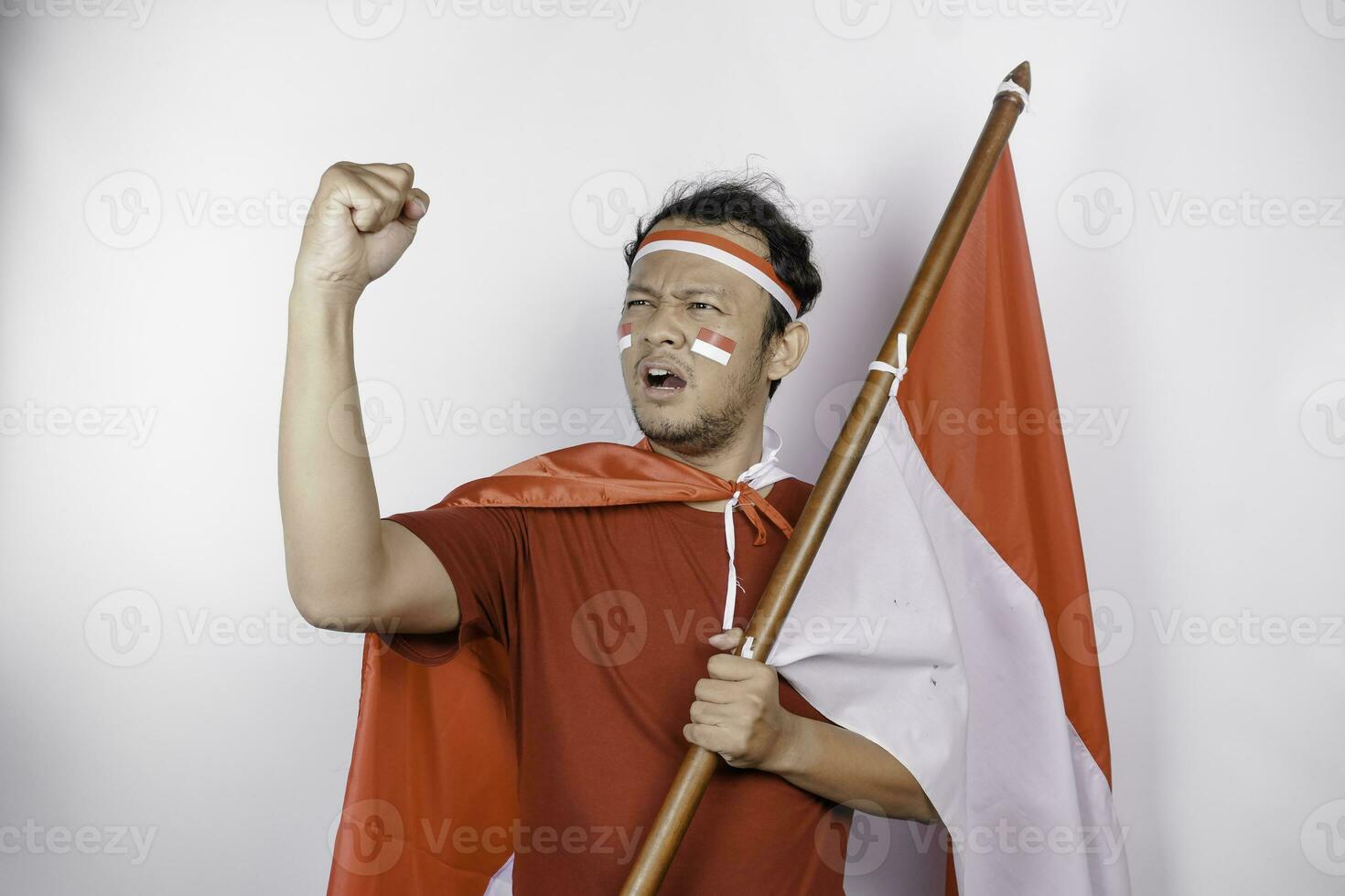 een jong Aziatisch Mens met een gelukkig geslaagd uitdrukking vervelend rood top en hoofdband terwijl Holding Indonesië's vlag, geïsoleerd door wit achtergrond. Indonesië's onafhankelijkheid dag concept. foto