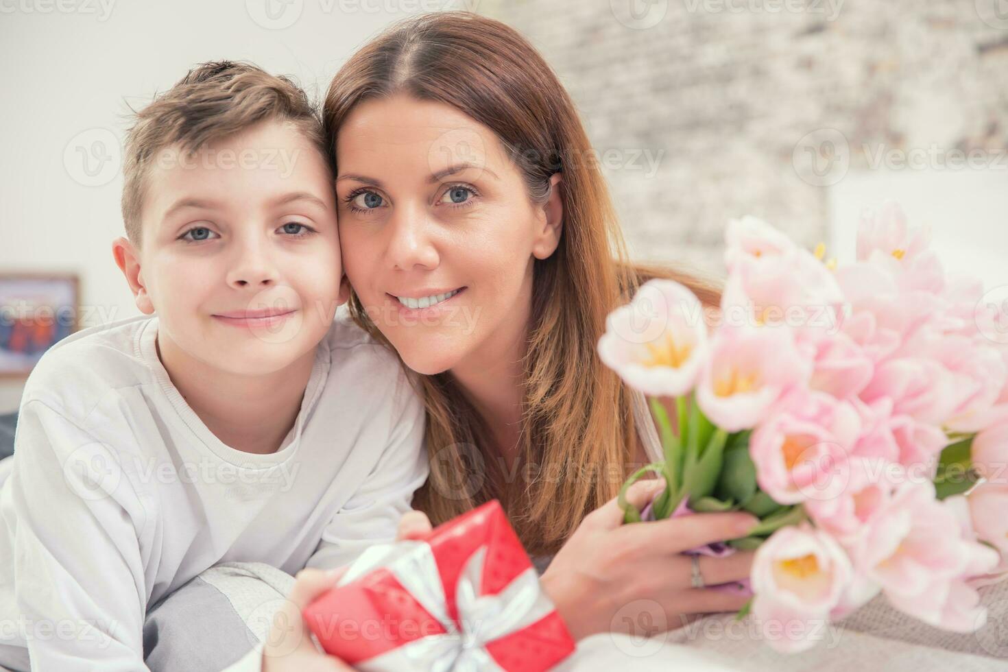 gelukkig moeder dag concept. mam met zoon Aan bed met geschenk en tulpen foto