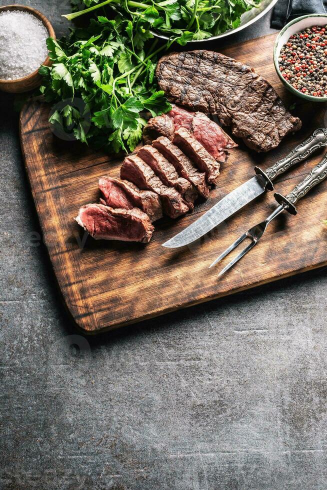 plakjes van sappig gegrild rundvlees steak met vork en mes Aan een slager bord foto