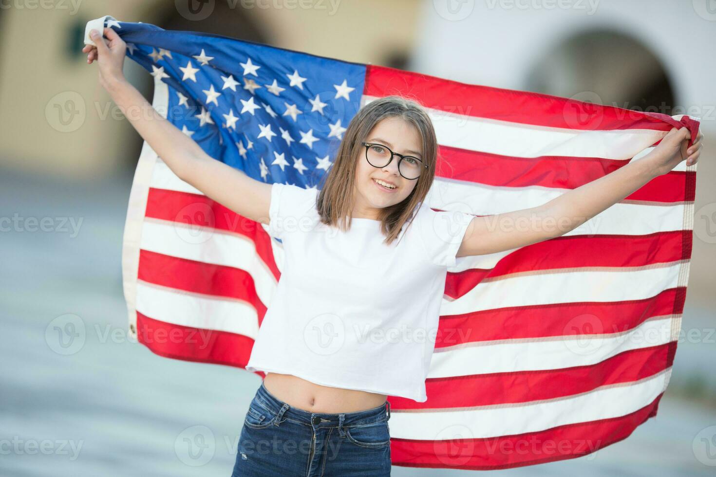 gelukkig jong Amerikaans school- meisje Holding en golvend in de stad met Verenigde Staten van Amerika vlag foto