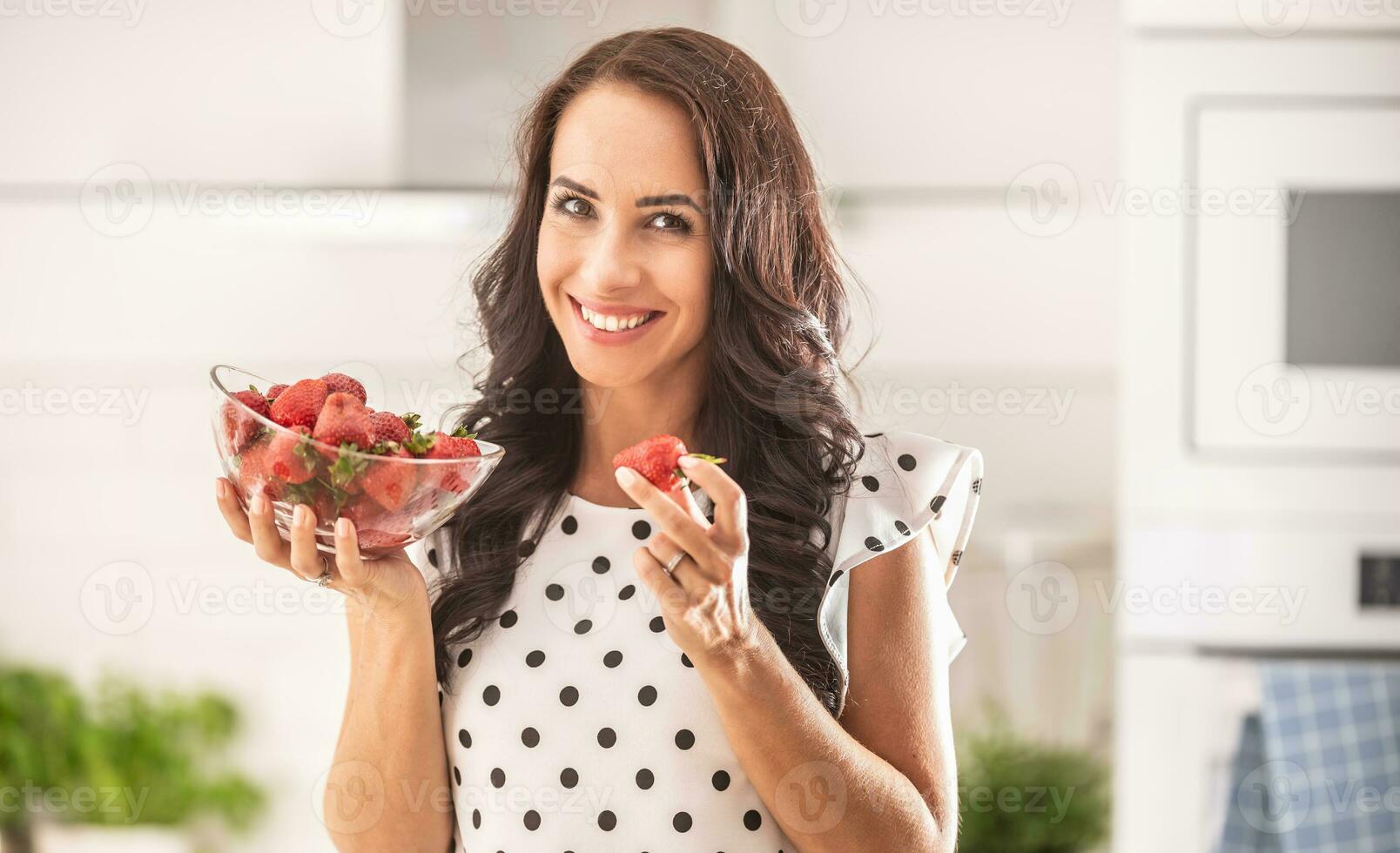 mooi meisje in stip jurk houdt een vers aardbei van een kom in haar hand- foto