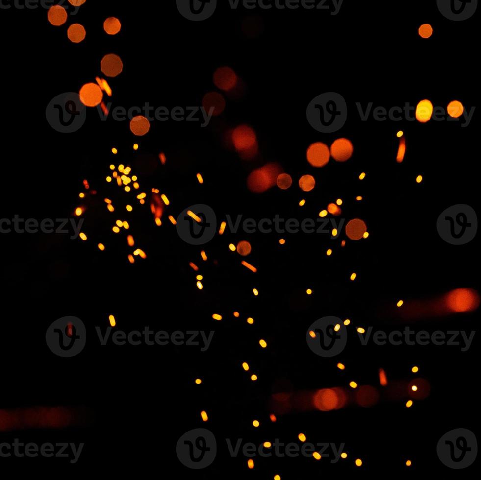 deeltjes brandende sintels vliegen en gloeien geïsoleerd in de nachtelijke hemel. heldere gele vonken op een zwarte achtergrond, gele heldere ronde bokeh. foto