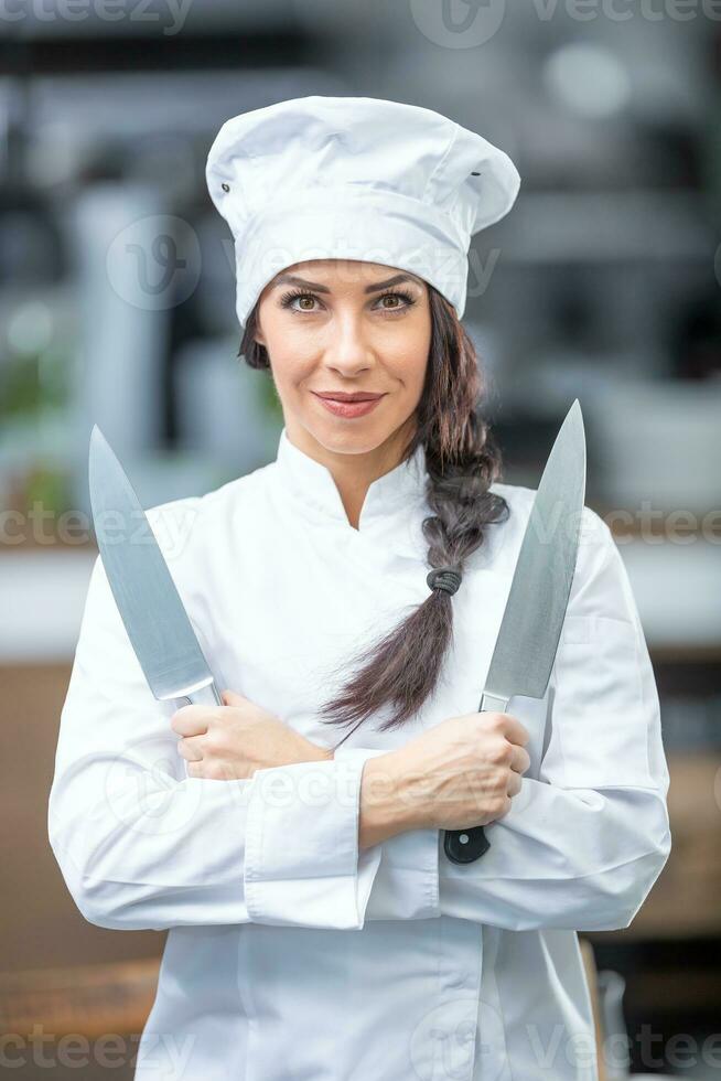 mooi vrouw chef staat in de keuken Holding twee messen glimlachen Bij de camera foto