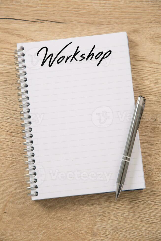 blanco spiraal notitieboekje met een werkplaats opschrift en leeg lijnen geplaatst Aan een houten tafel en een metalen zilver pen gepositioneerd Aan top van het foto