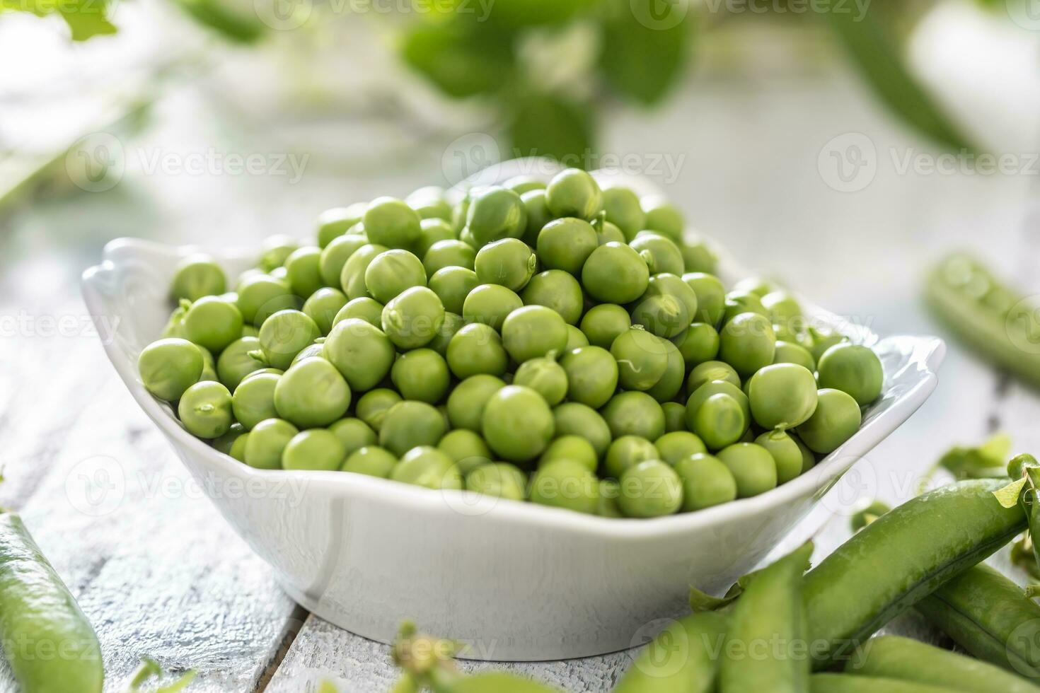 groen rauw erwten en peulen in pocelain boog geïsoleerd Aan houten tafel foto