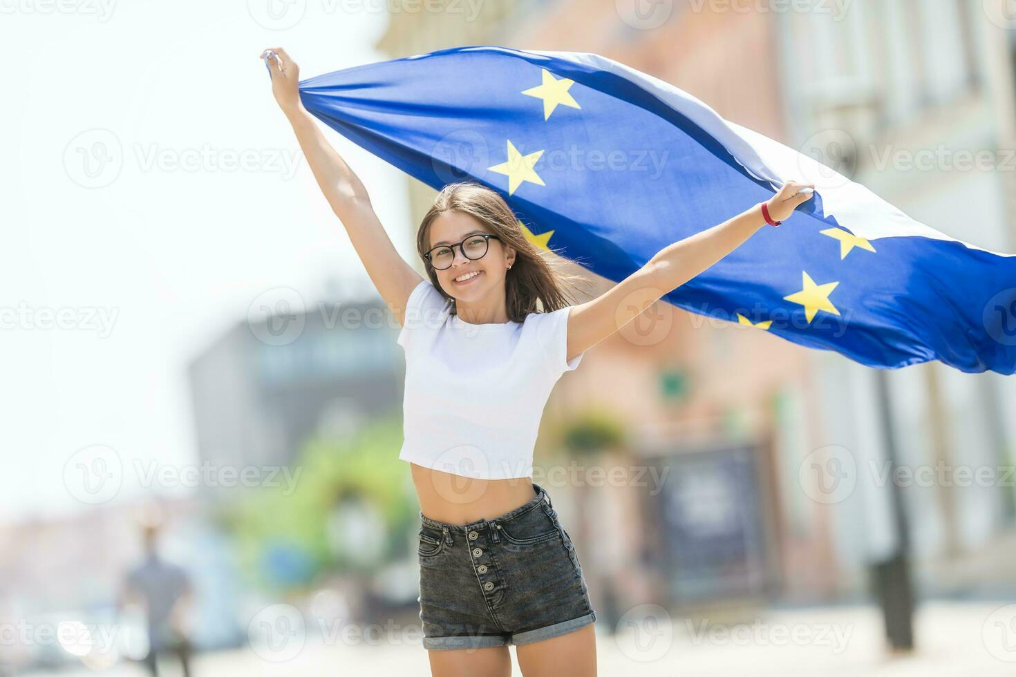 schattig gelukkig jong meisje met de vlag van de Europese unie in de straten ergens in Europa foto