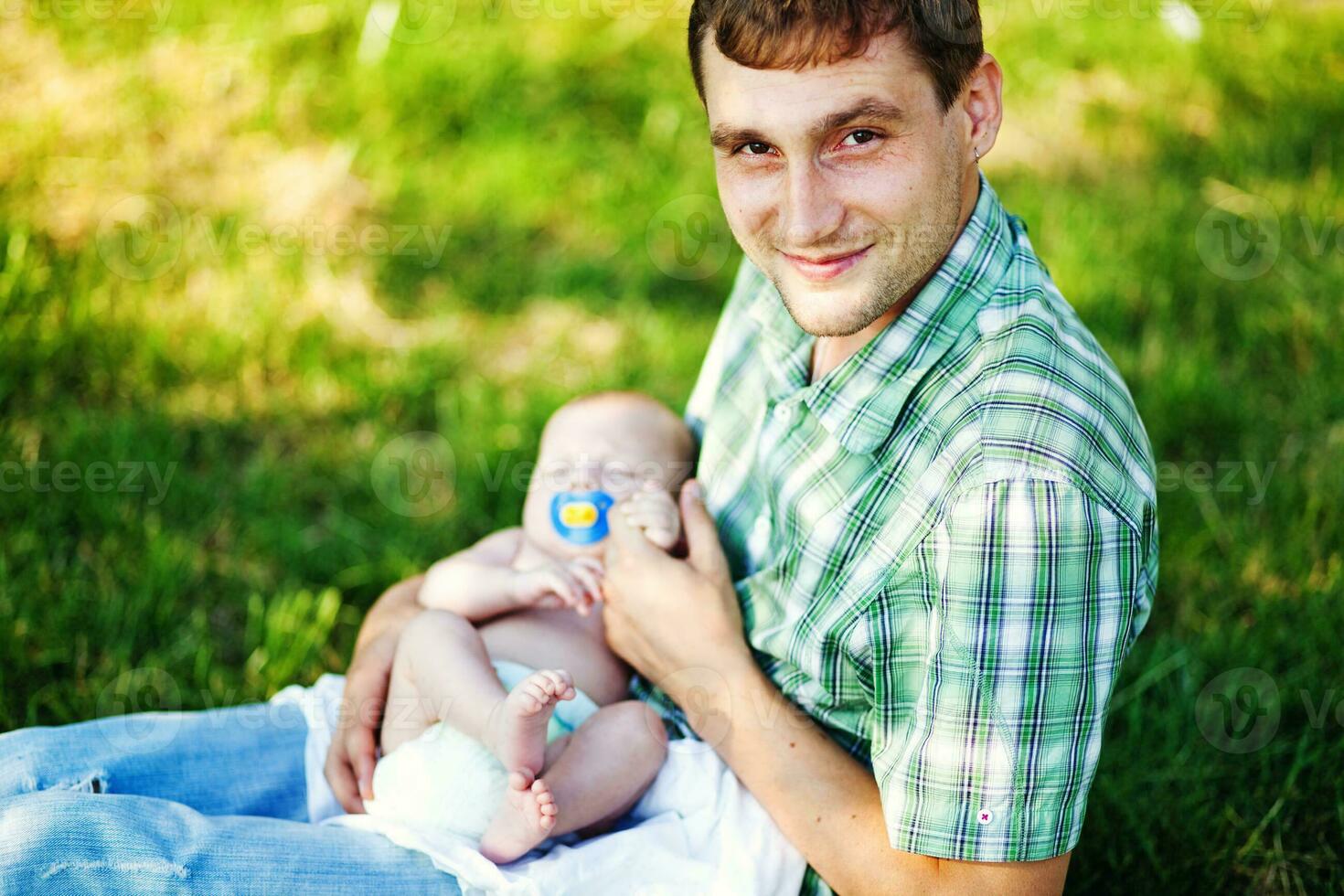 een Mens is Holding een baby terwijl zittend in de gras foto