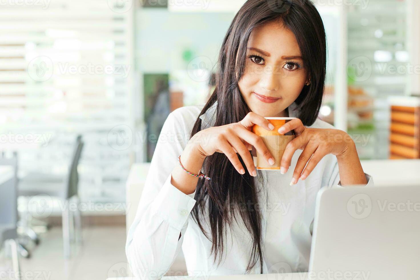 een vrouw Holding een koffie kop in voorkant van haar laptop foto