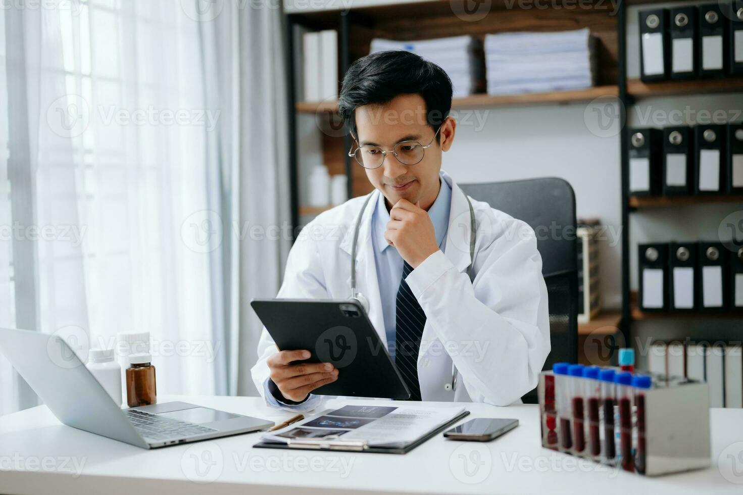 medisch technologie concept. Aziatisch dokter werken met mobiel telefoon en stethoscoop in modern kantoor foto