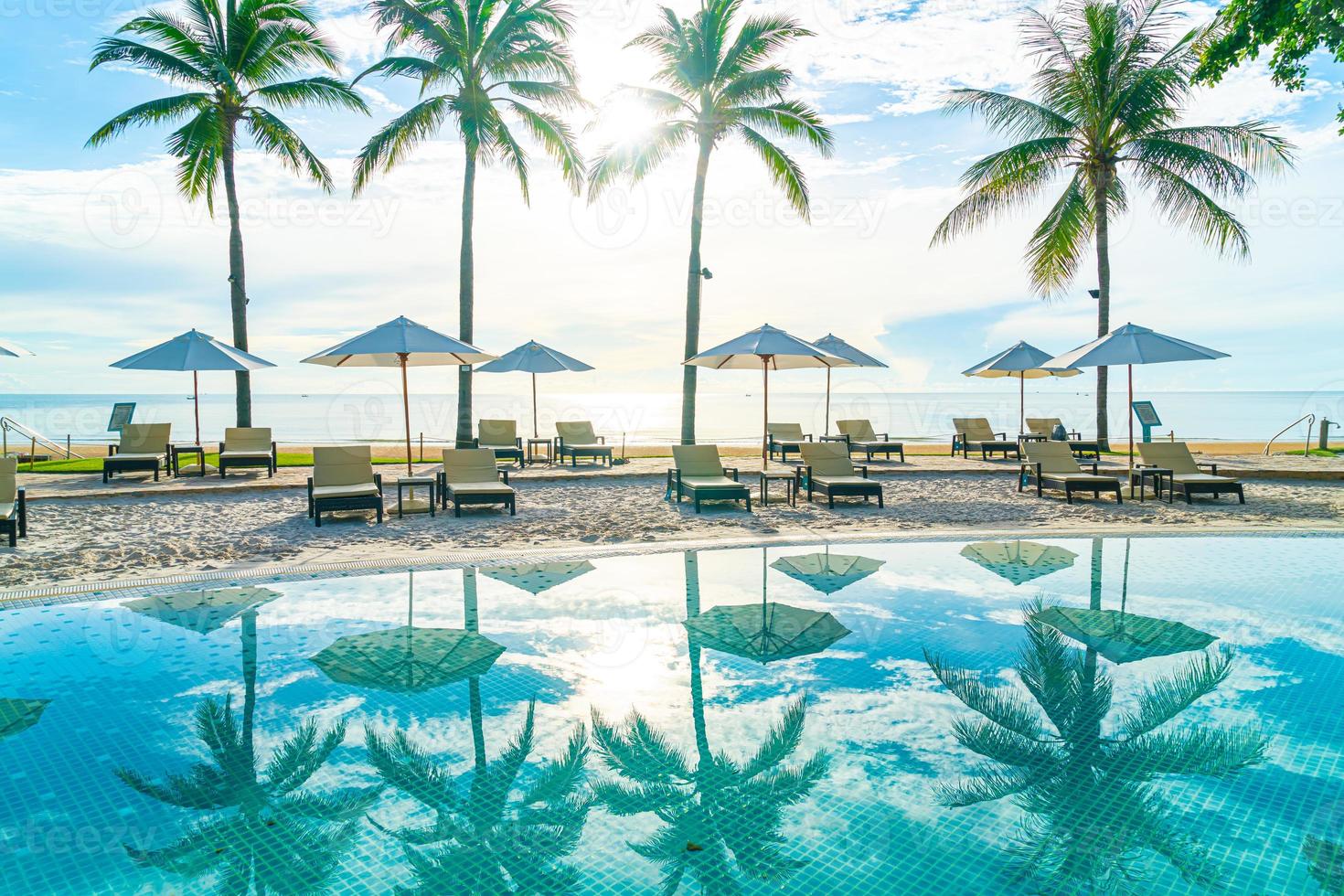 mooie luxe parasol en stoel rond buitenzwembad in hotel en resort met kokospalm op zonsondergang of zonsopgang foto