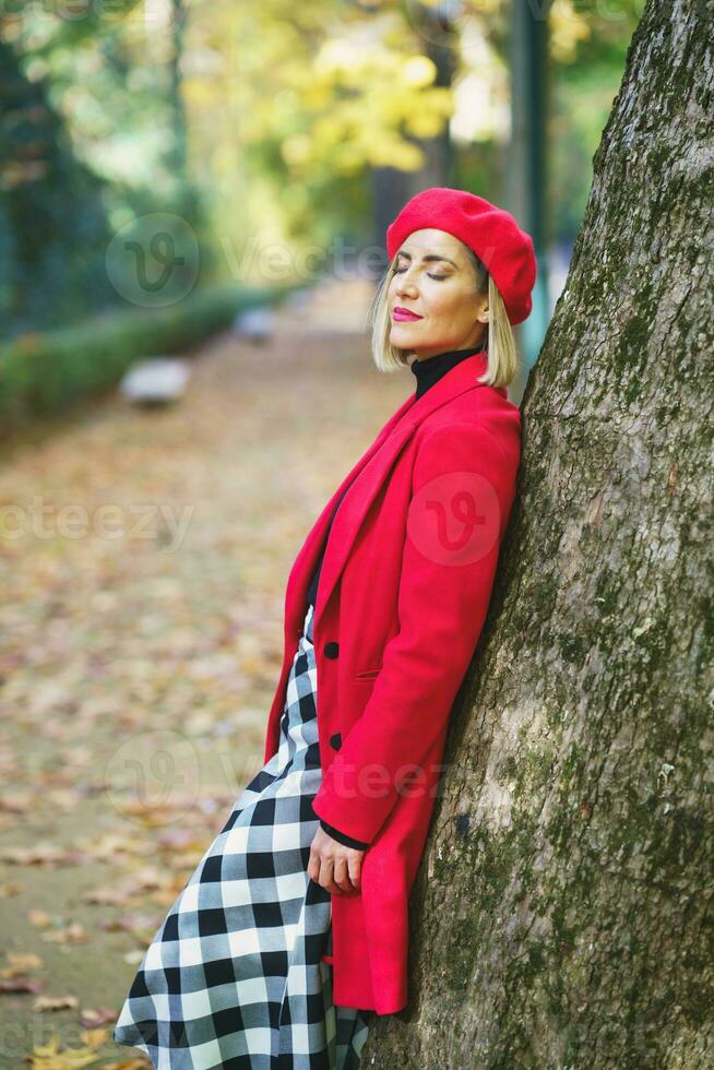 teder vrouw in rood bovenkleding leunend Aan boom foto