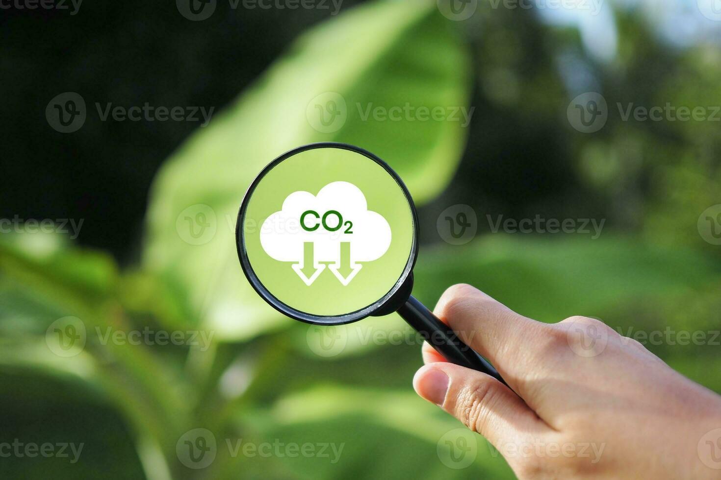 hand- Holding een vergroten glas met co2 vermindering icoon, Nee koolstof dioxide uitstoot. koolstof credits naar begrenzing globaal opwarming.co2 emissie concept. groen industrieën bedrijf concept. netto nul uitstoot. foto