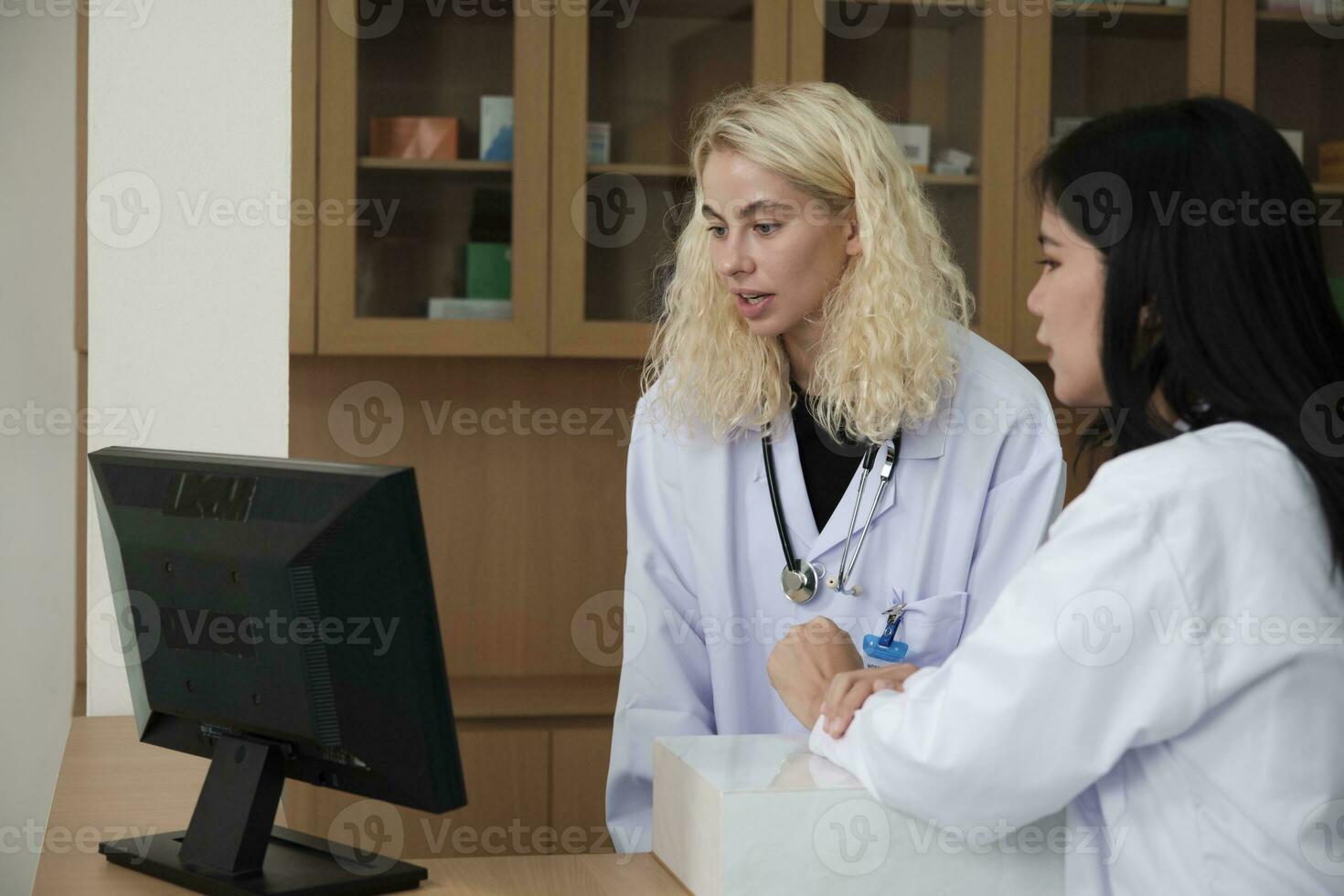 twee professioneel medisch personeel, Aziatisch vrouw dokter, en wit apotheker besproken behandeling geneeskunde voorschriften Bij teller van de apotheek afdeling in ziekenhuis kliniek. foto