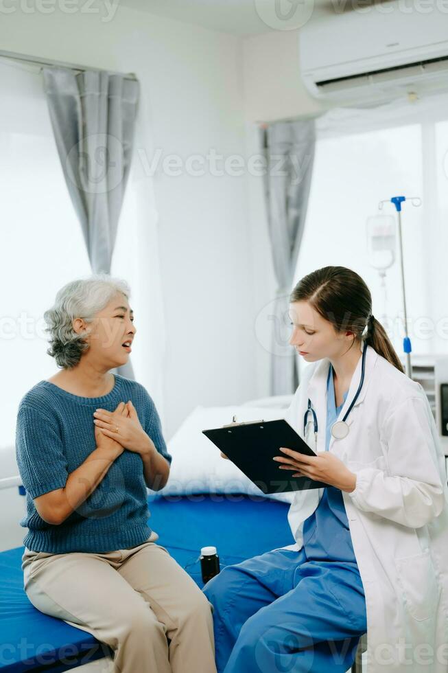 vriendelijk vrouw hoofd verpleegster maken rondes doet controle Aan geduldig resting in bed. ze cheques tablet terwijl Mens ten volle herstellen na geslaagd chirurgie in ziekenhuis foto