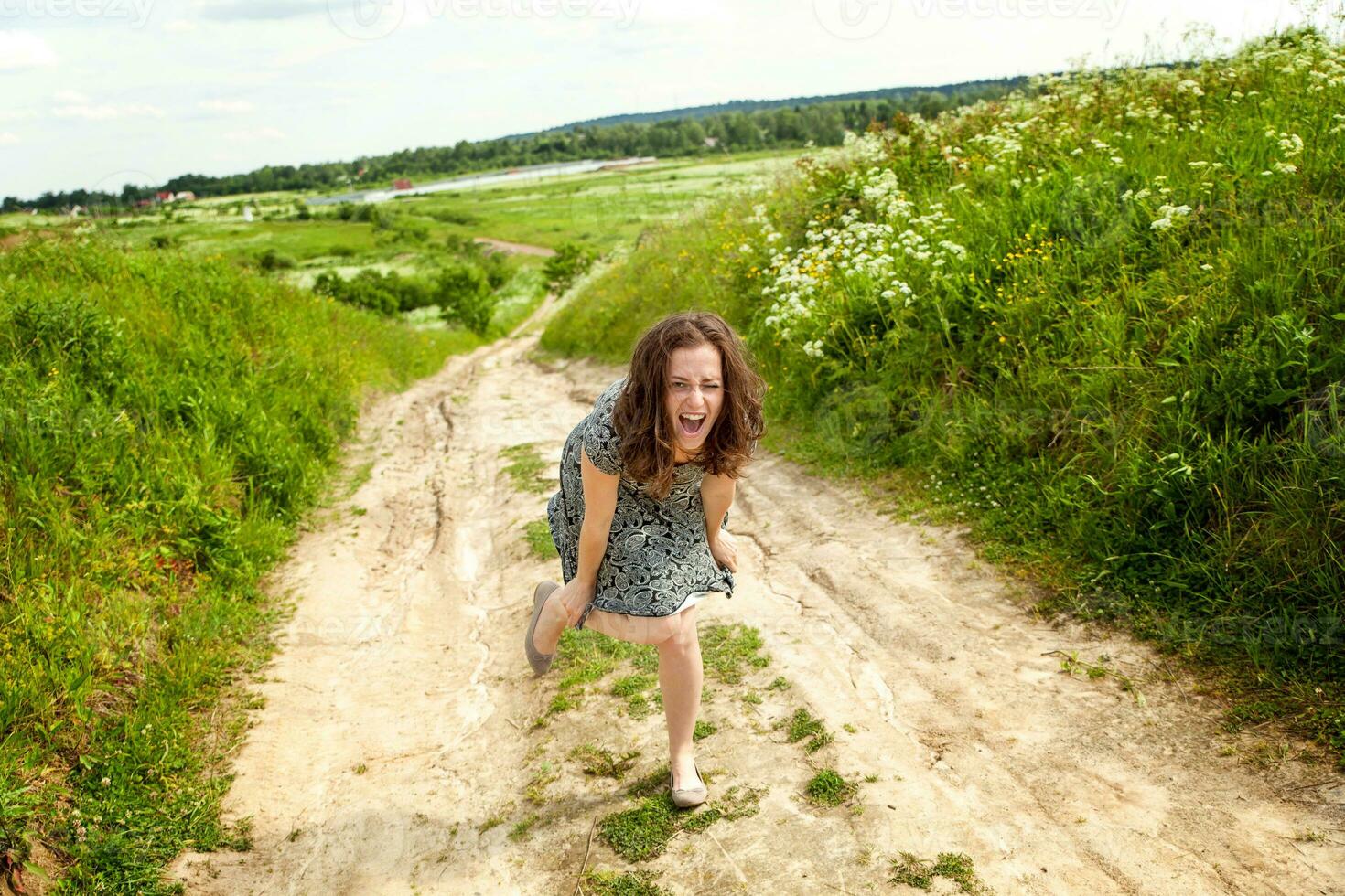 schoonheid meisje buitenshuis genieten van natuur. mooi vrouw jumping Aan zomer veld- met bloeiend wild bloemen, zon licht. vrij gelukkig vrouw. foto