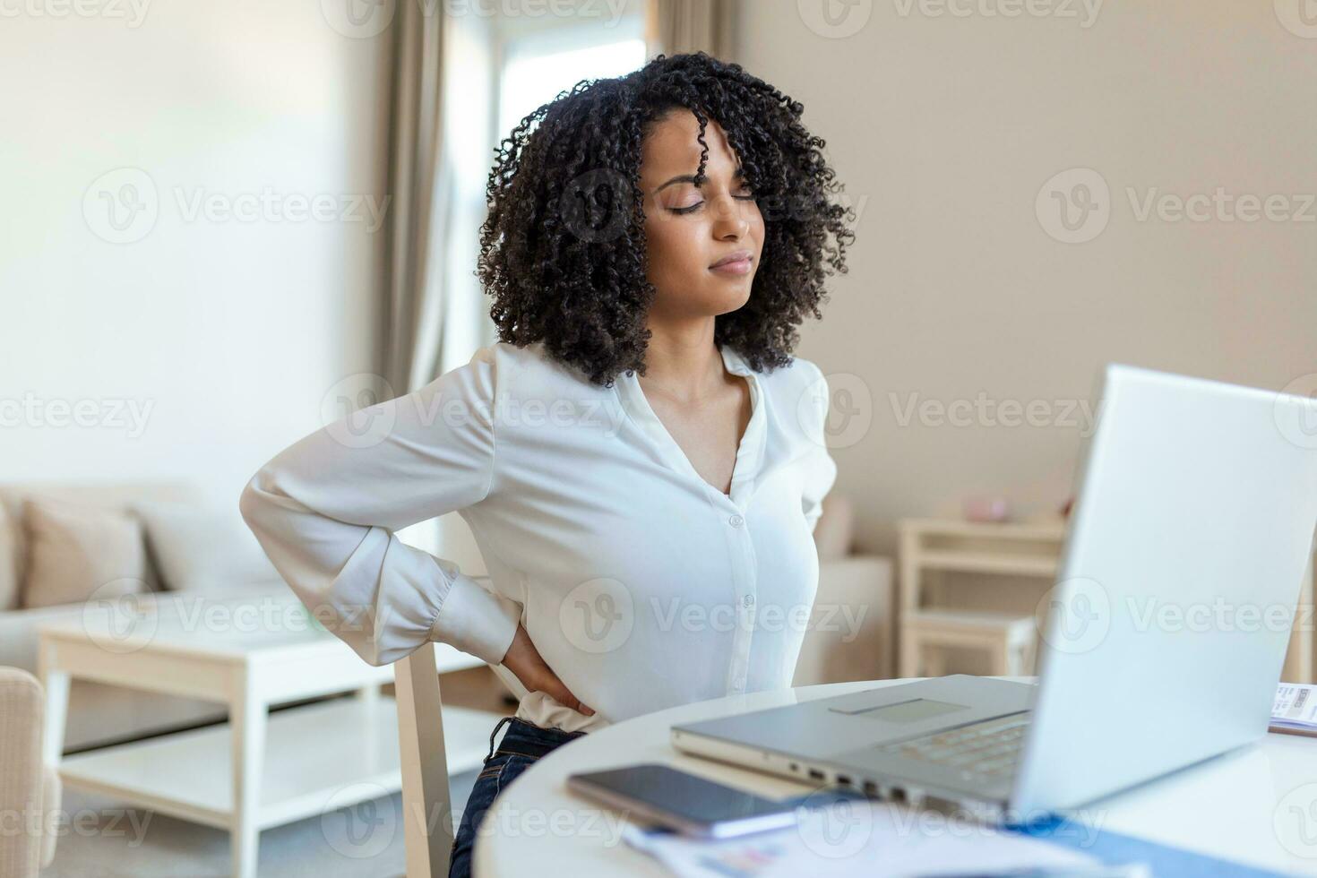 terug pijn slecht houding vrouw zittend in kantoor. jong afro vrouw lijden van terug pijn terwijl werken Aan laptop Bij huis foto